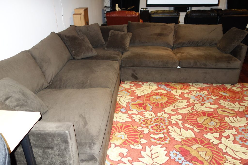 A plush grey sectional sofa beside a bold coral and cream floral rug