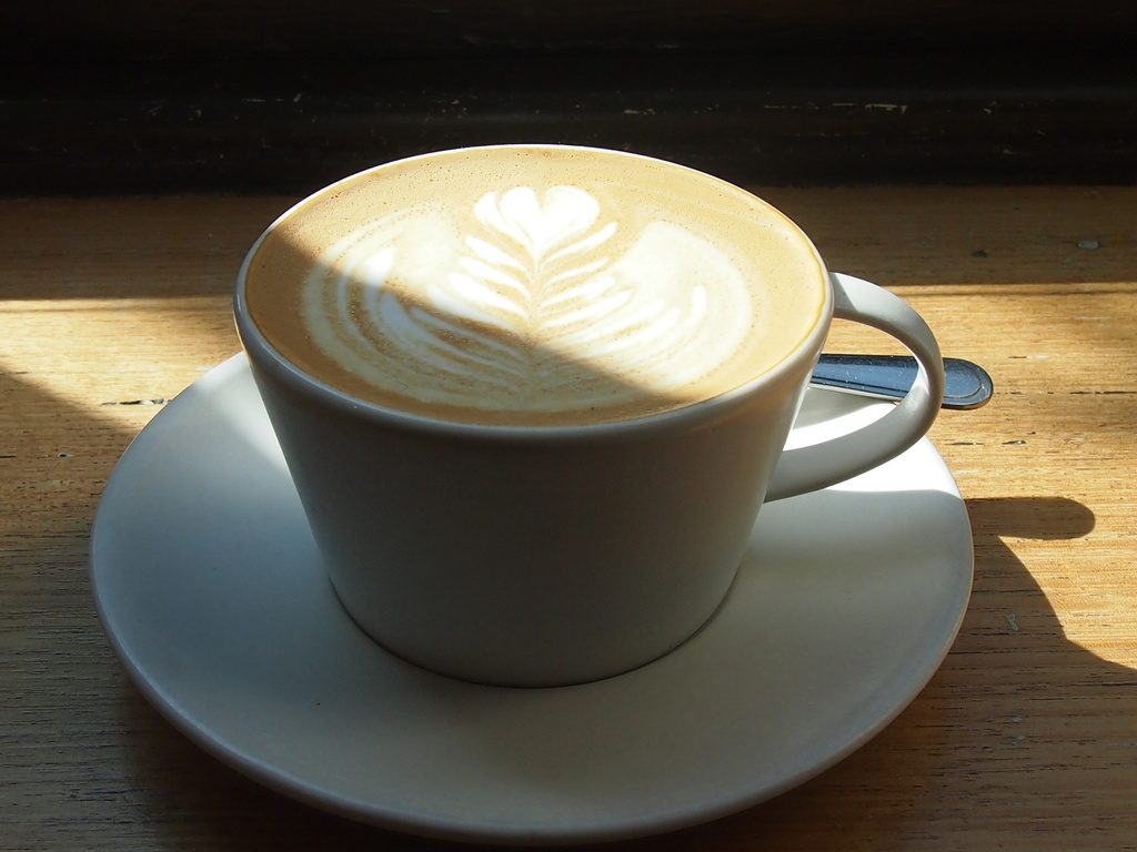 A latte with heart-shaped foam art in a white cup, lit by soft window light