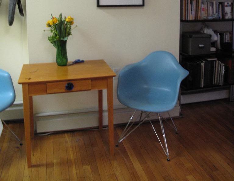 A pine side table with a vase of yellow tulips beside two pale blue chairs