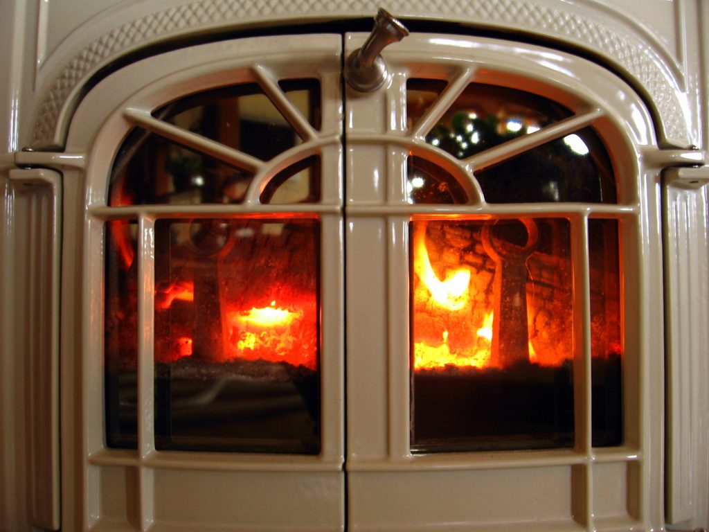 A cream enamel wood stove with a fire glowing behind its arched glass doors