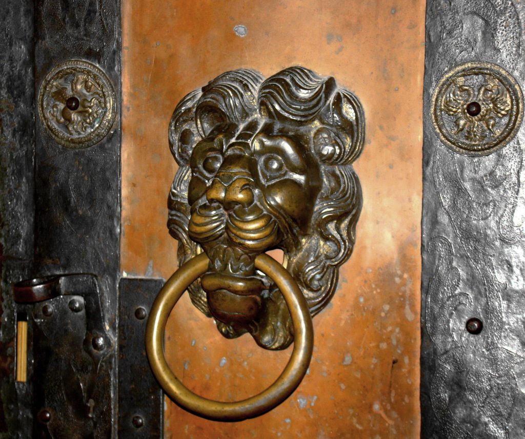 A brass lion door knocker on a heavy wooden door with iron fittings